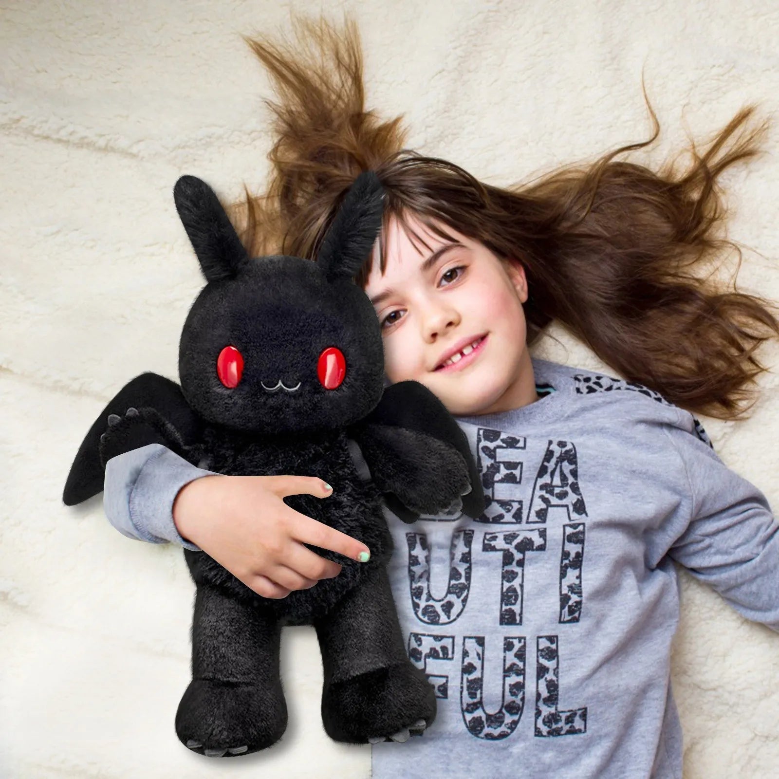 Child holding a black plush toy with red eyes on a white blanket