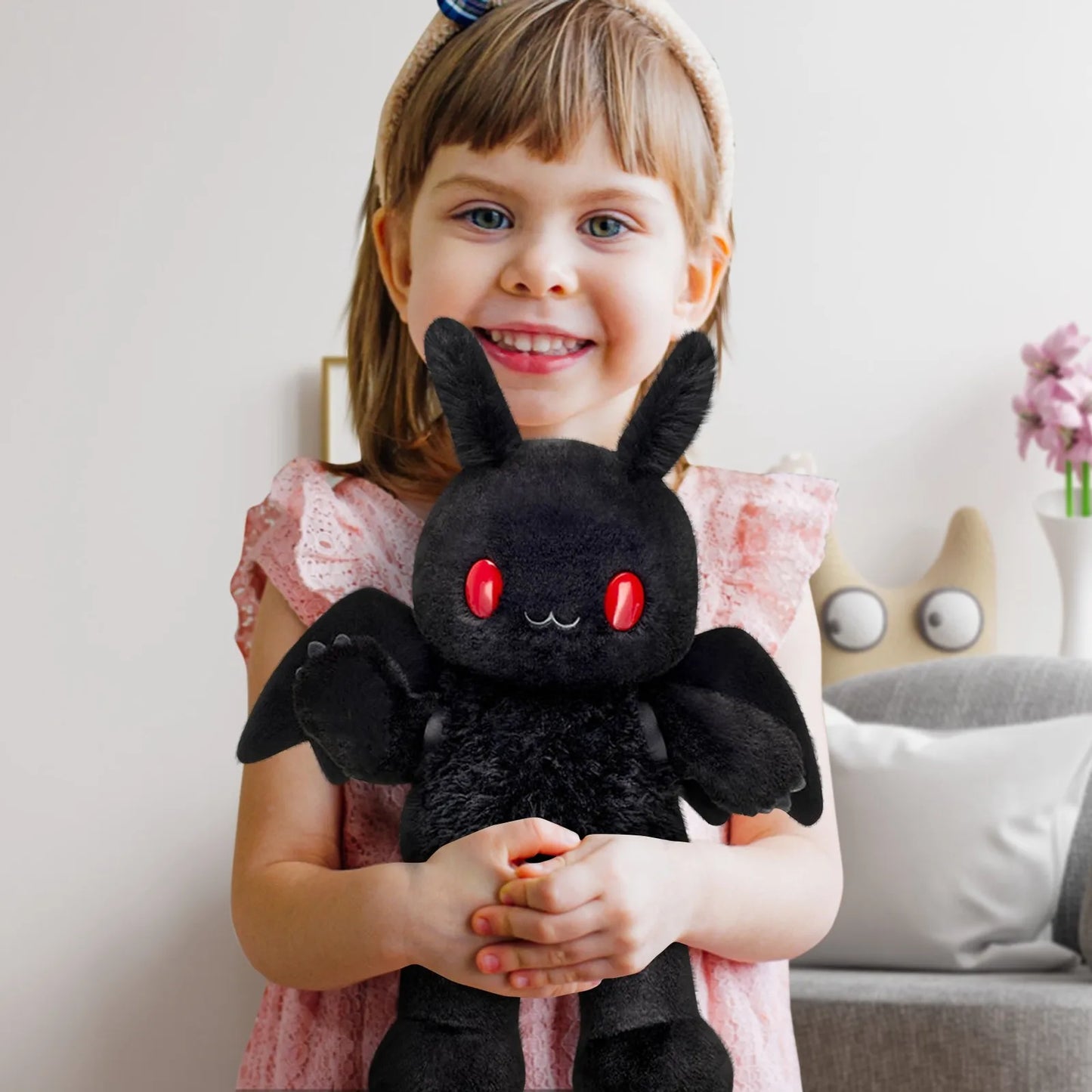 Child holding a black plush toy with red eyes in a room setting.